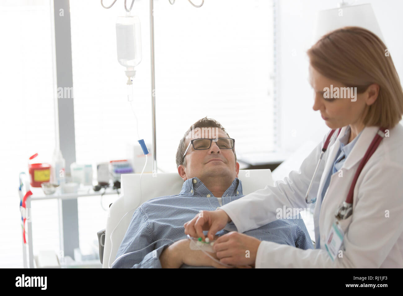 Doctor adjusting saline IV drip for mature patient in hospital Stock Photo