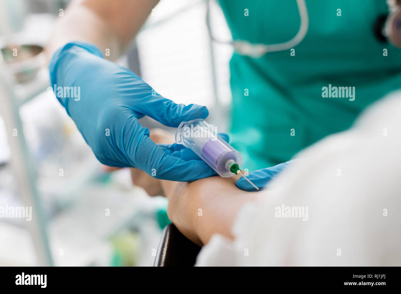 Nurse wearing gloves while injecting patient at hospital Stock Photo