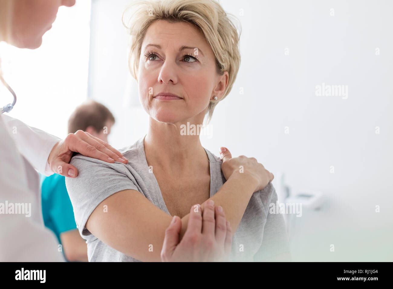 Doctor assisting mature patient in stretching arm at hospital Stock Photo