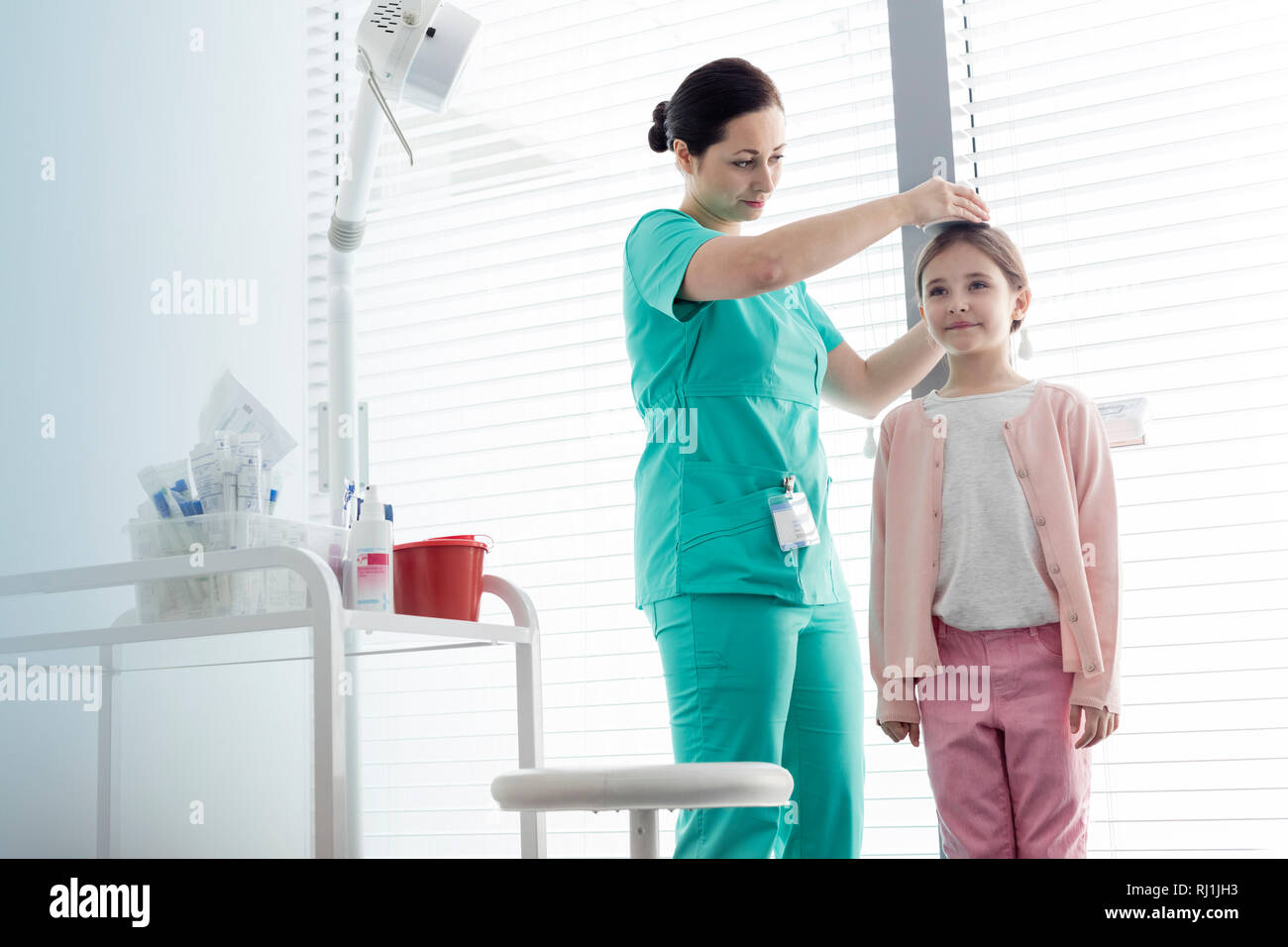 Nurse measuring height of girl against window at examination room Stock Photo