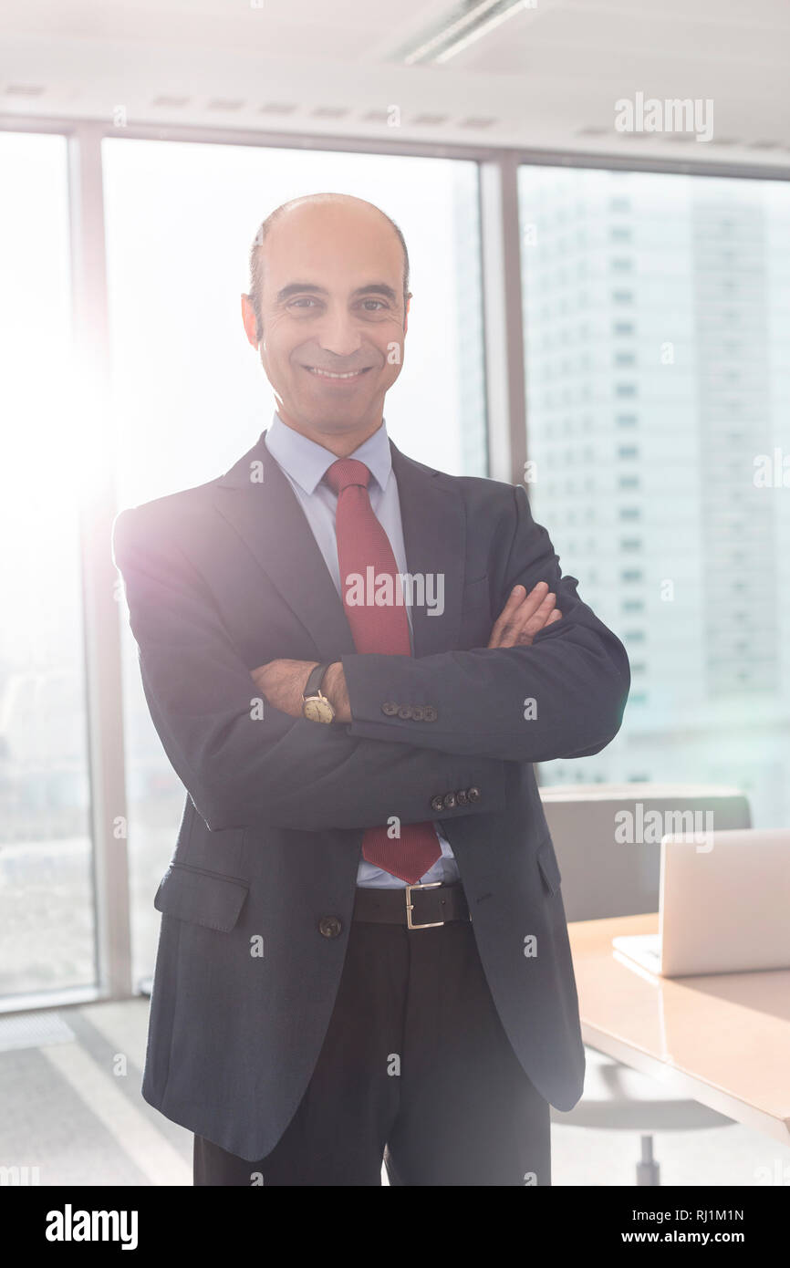 Portrait of smiling businessman standing with arms crossed in boardroom ...