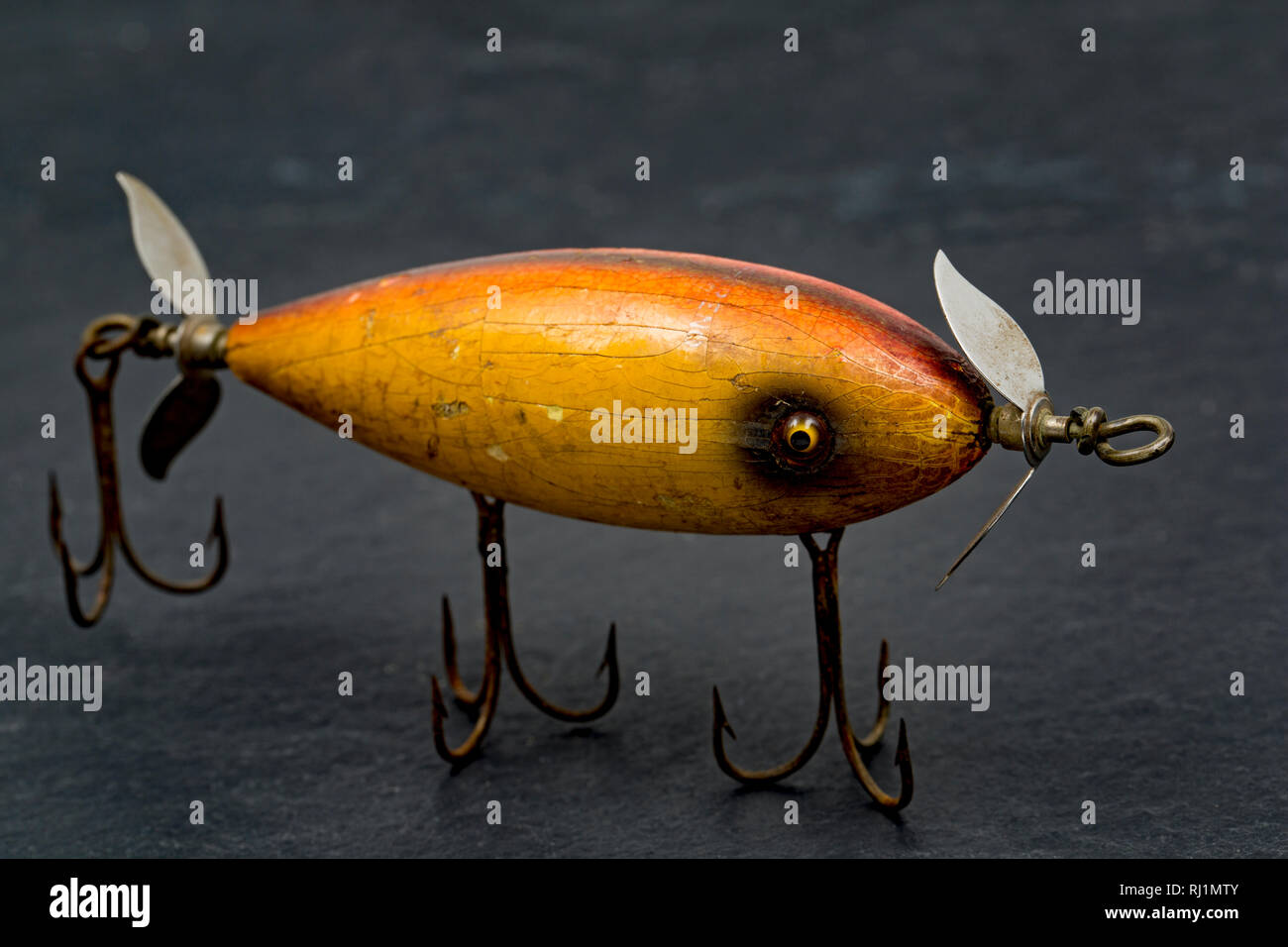 An old, wooden South Bend lure equipped with three treble hooks photographed on a dark, slate background. These lures were designed to float on the su Stock Photo