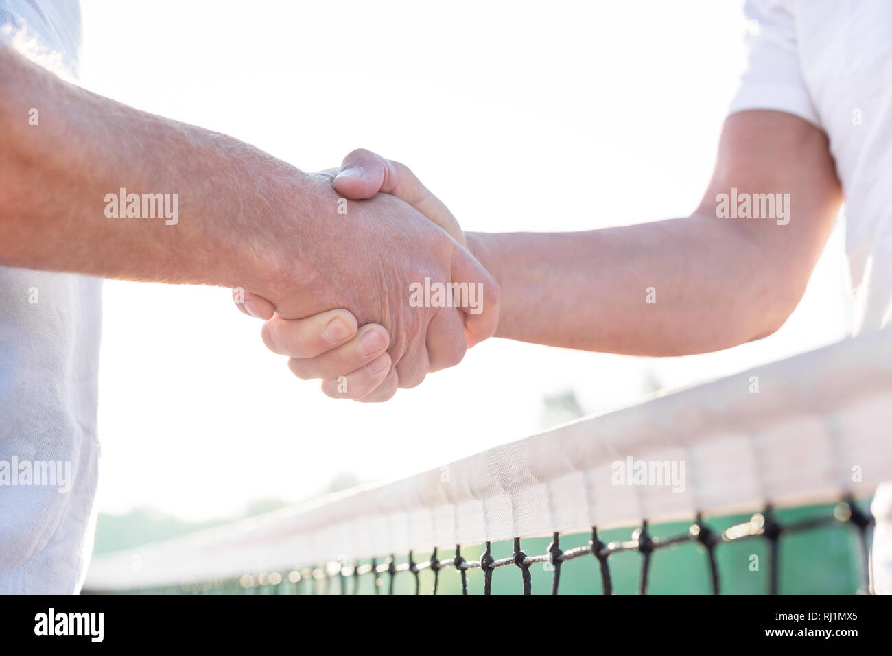 Midsection of men shaking hands while standing at tennis court against clear sky Stock Photo
