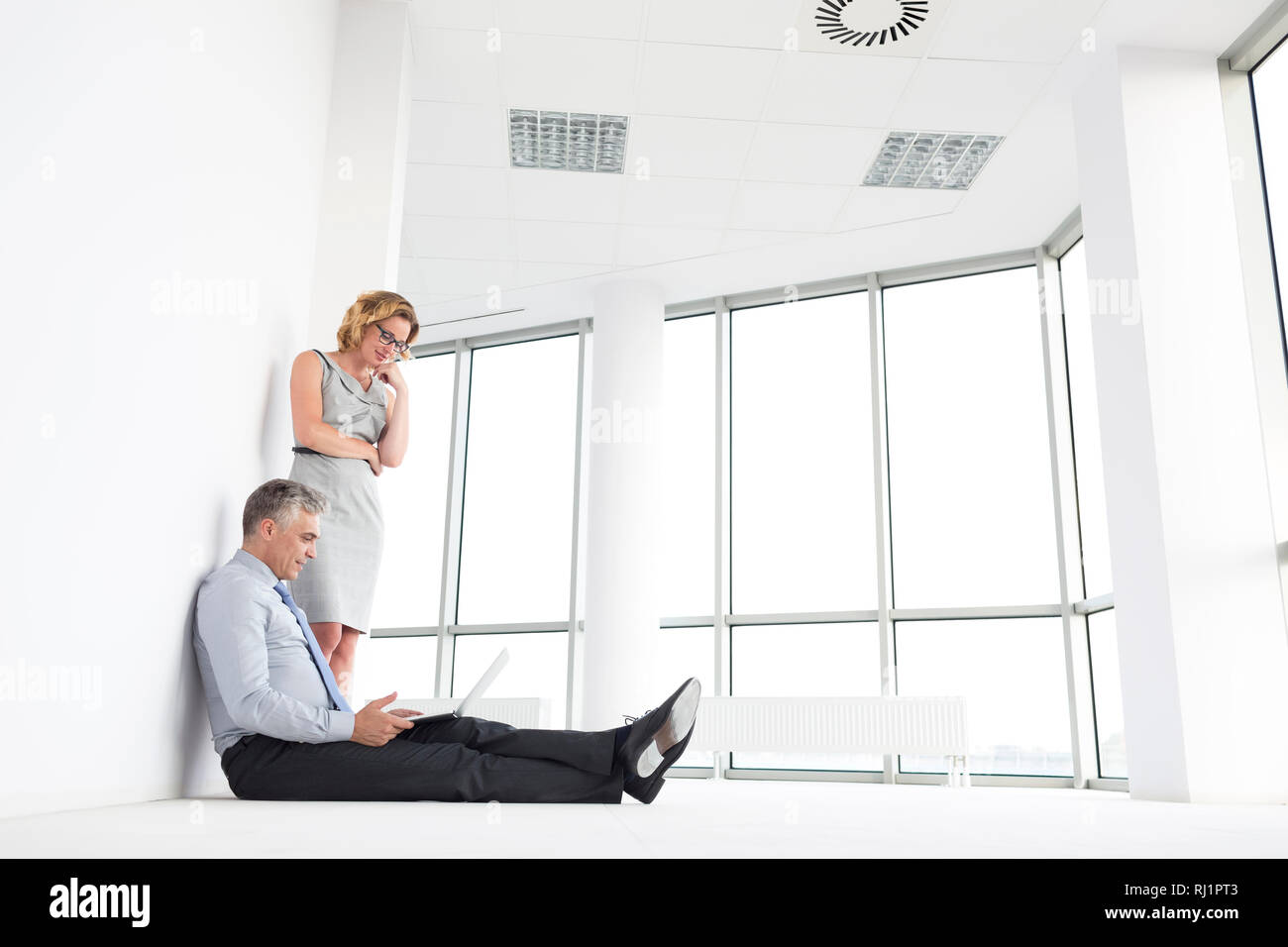 Businesswoman standing by businessman using laptop at new office Stock Photo