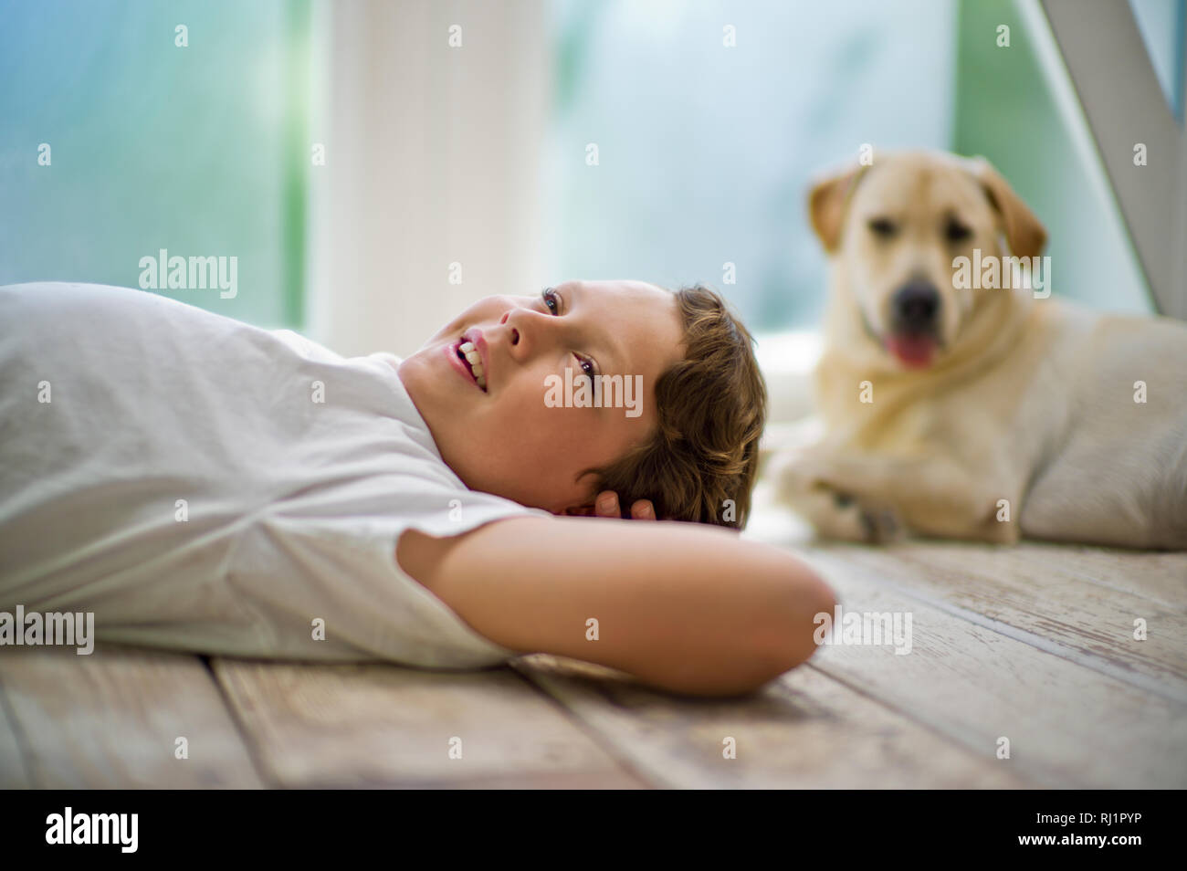 Smiling teenage boy daydreaming while lying with hands behind his head on a hardwood floor. Stock Photo