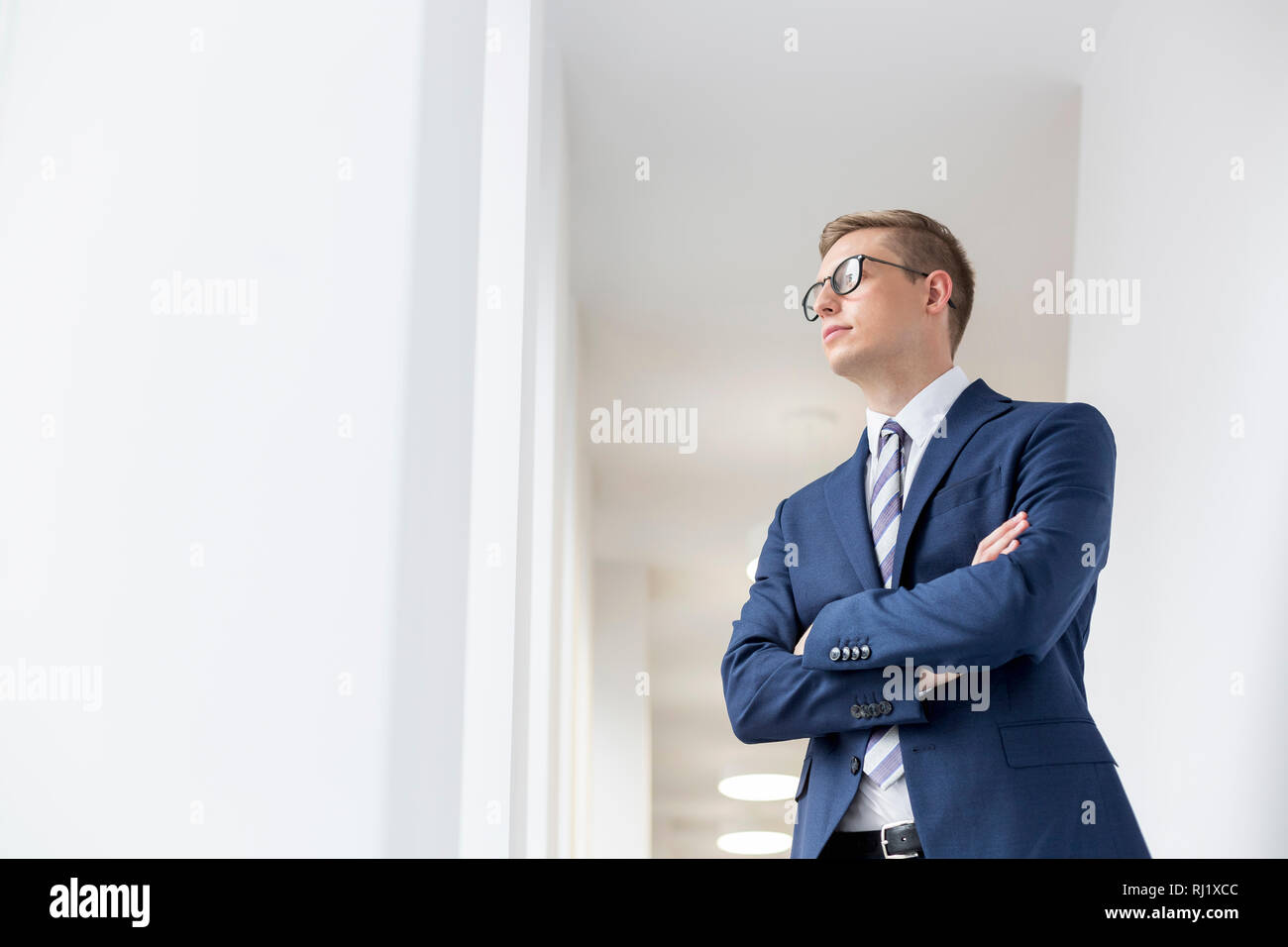 Young thoughtful businessman standing with arms crossed looking away in ...