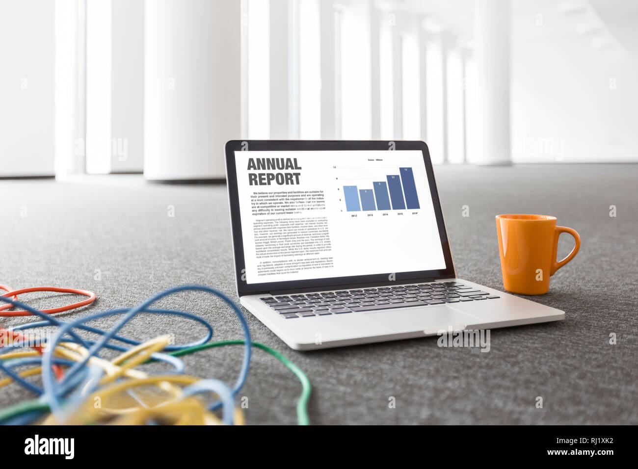 Annual report graph on laptop by coffee mug and cables at new empty office Stock Photo
