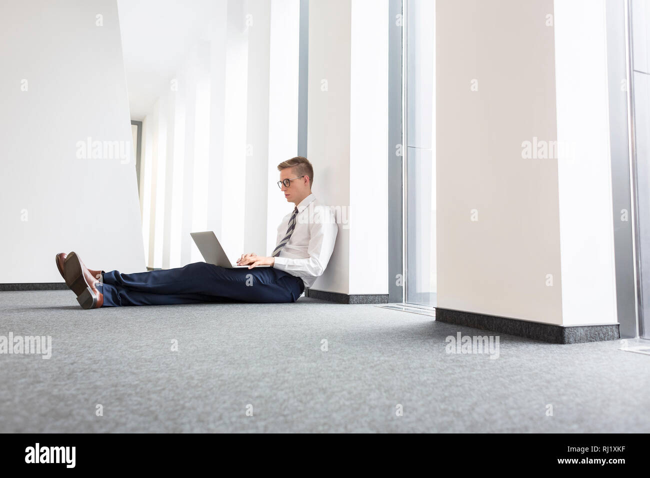 Young businessman using laptop while sitting on floor at office Stock Photo