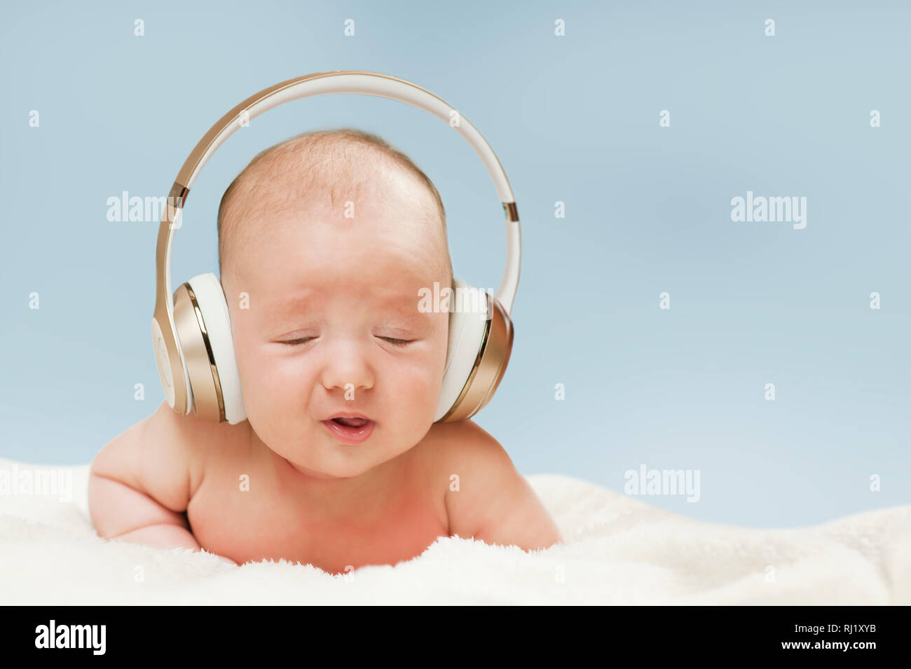 beautiful newborn baby in big headphones listening to music, isolated on blue background Stock Photo