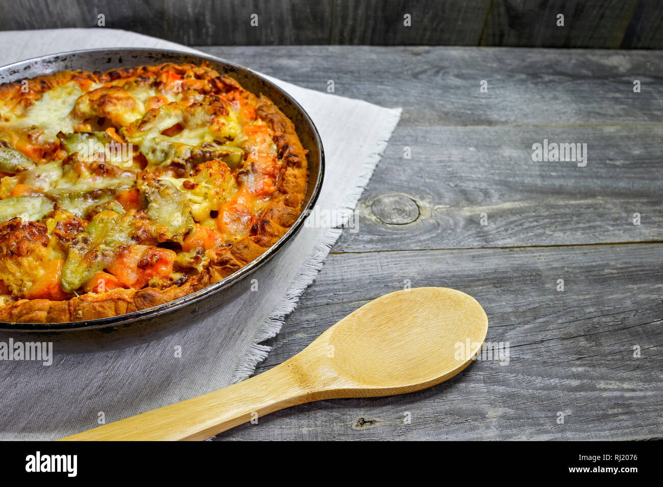 Pie with vegetables and cheese in a vintage pan with a wooden spoon on a white linen napkin on wooden rustic background Stock Photo