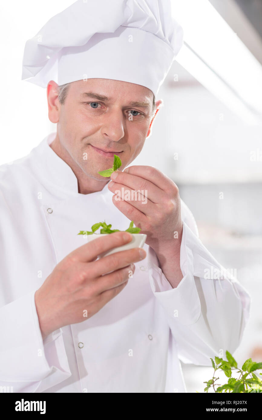 Confident mature chef smelling herb leaves in kitchen at restaurant Stock Photo