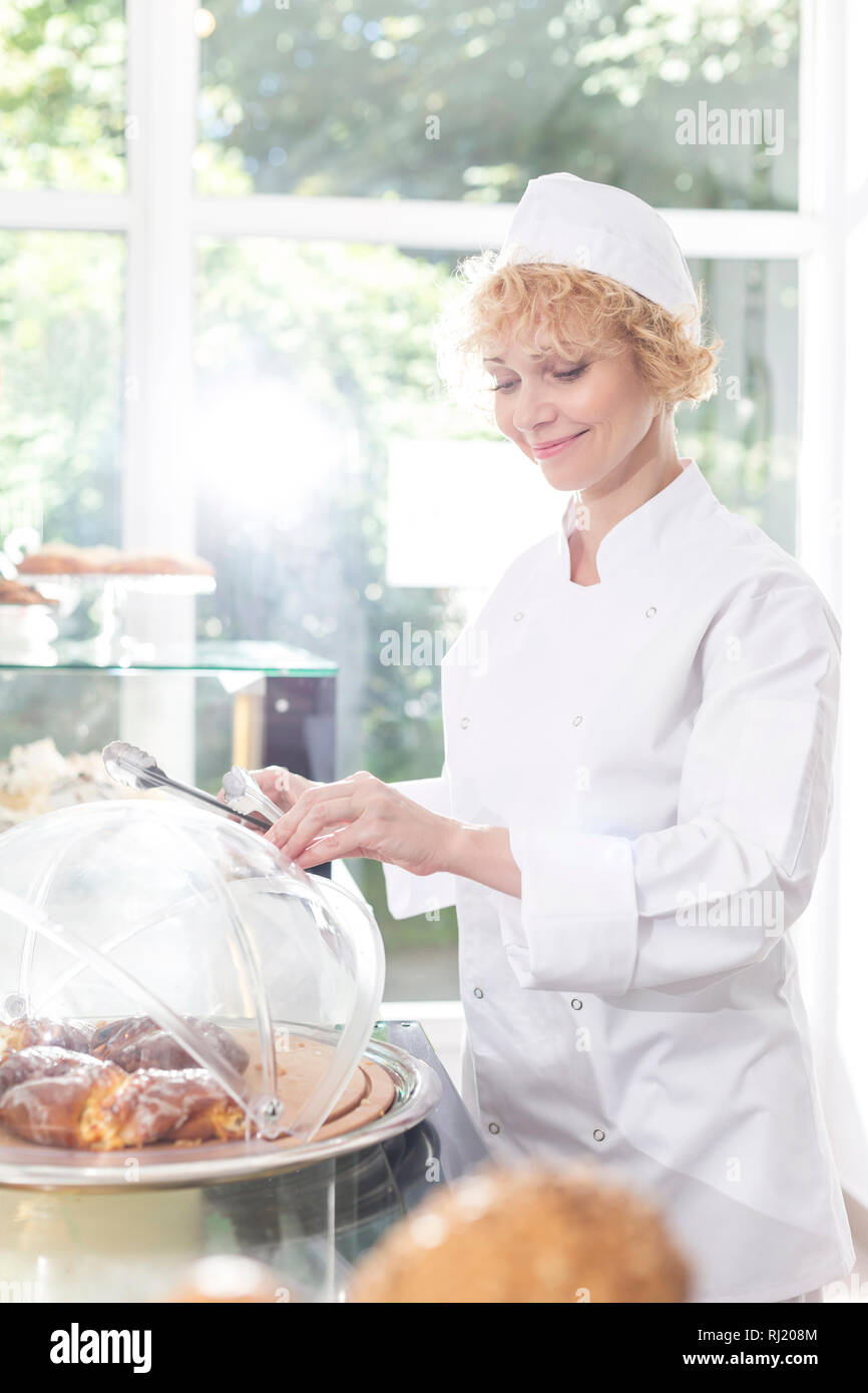 Smiling mature chef arranging fresh sweet food in container at restaurant counter Stock Photo