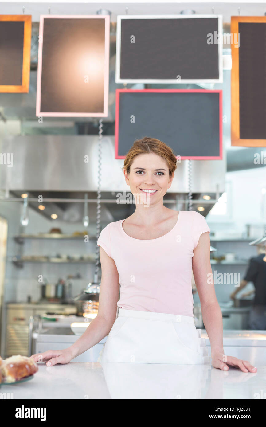 Portrait of smiling young waitress standing at counter in restaurant Stock Photo