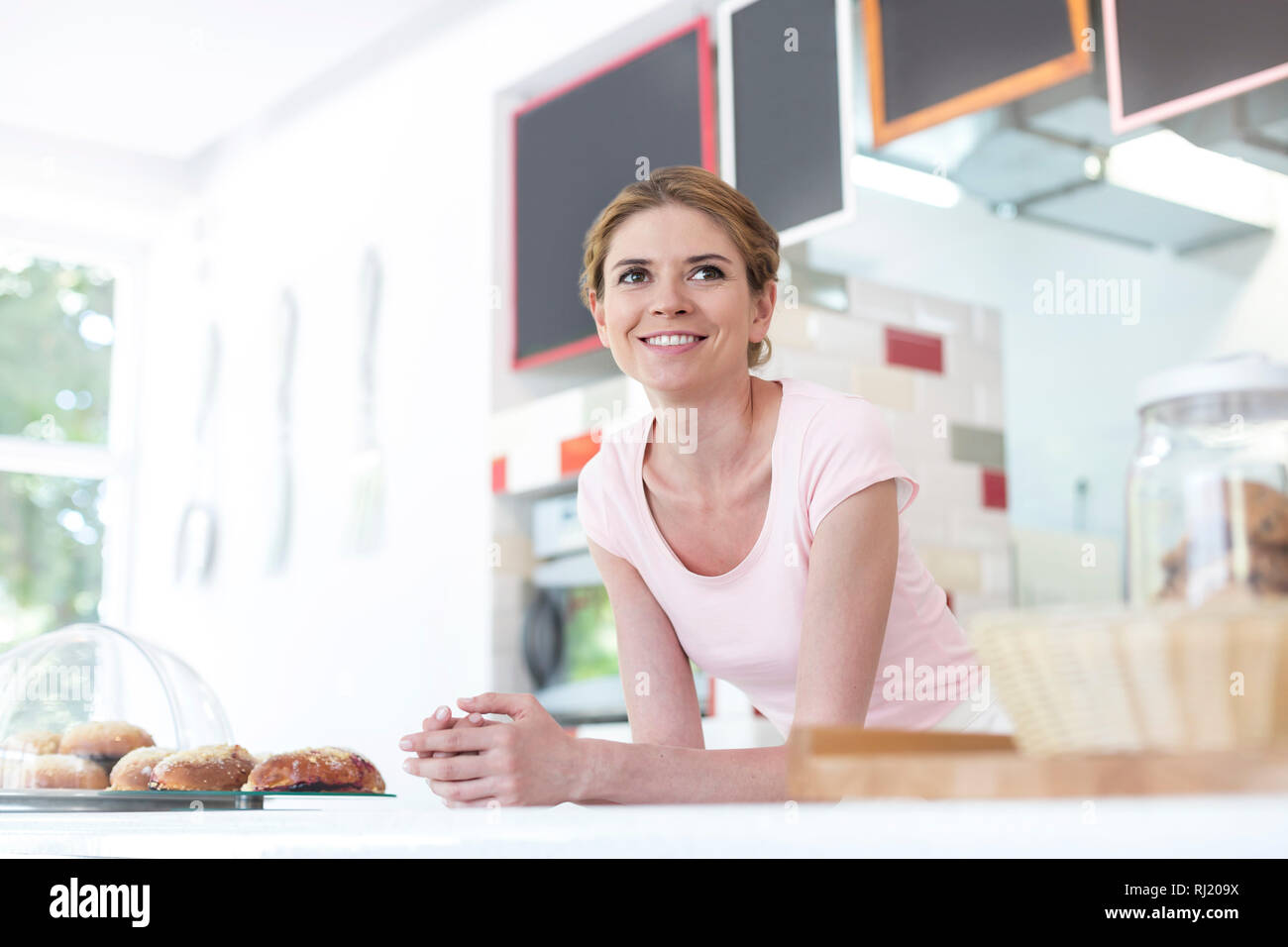 Smiling young waitress leaning on counter at restaurant Stock Photo