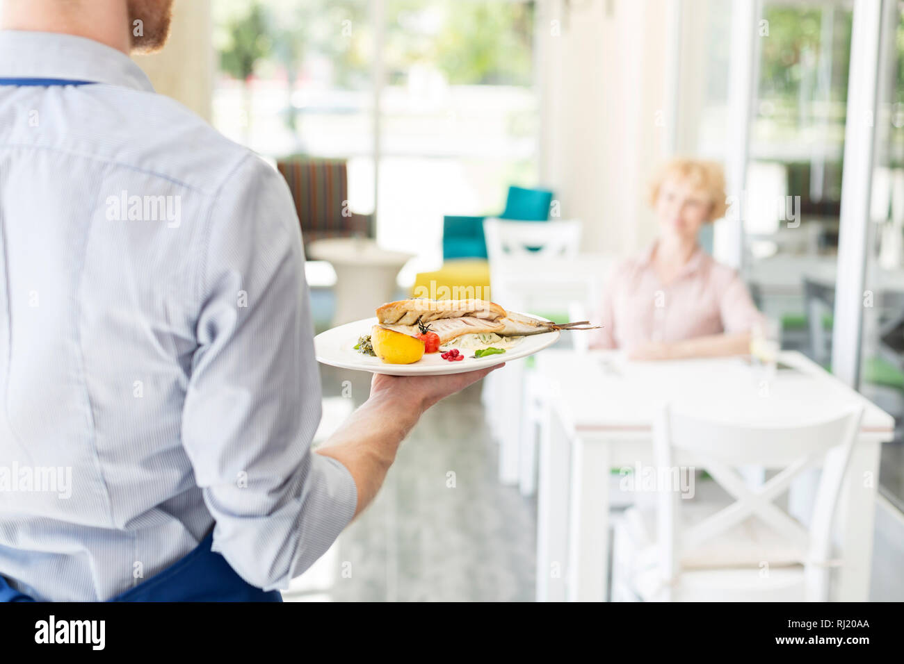 Midsection of waiter serving lunch to mature customer sitting at table