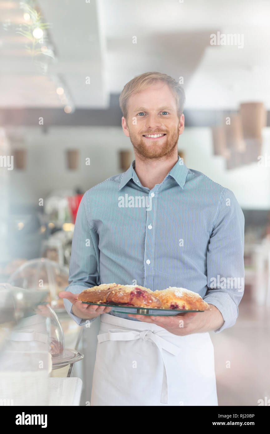 Portrait of smiling young waiter holding fresh bread in tray at restaurant Stock Photo