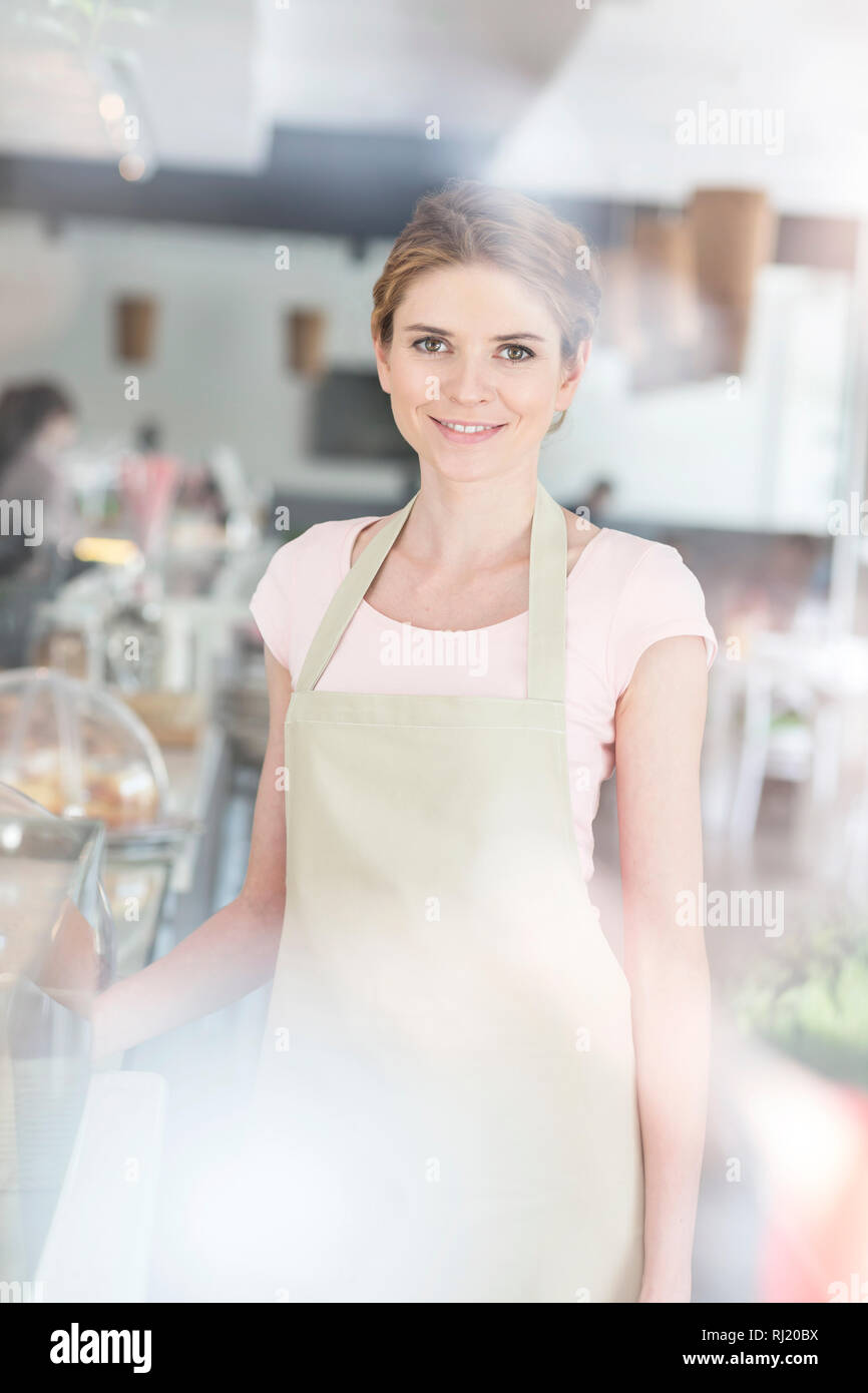 Portrait of smiling beautiful young waitress standing by counter at restaurant Stock Photo