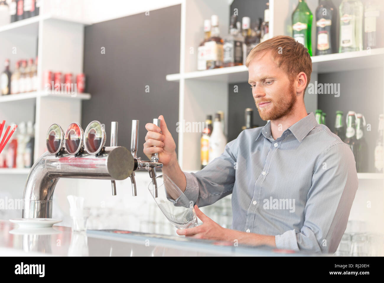 Young Waiter Filling Glass From Beer Tap At Restaurant Stock Photo