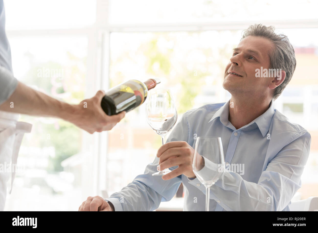 Young waiter serving wine to mature customer at restaurant Stock Photo