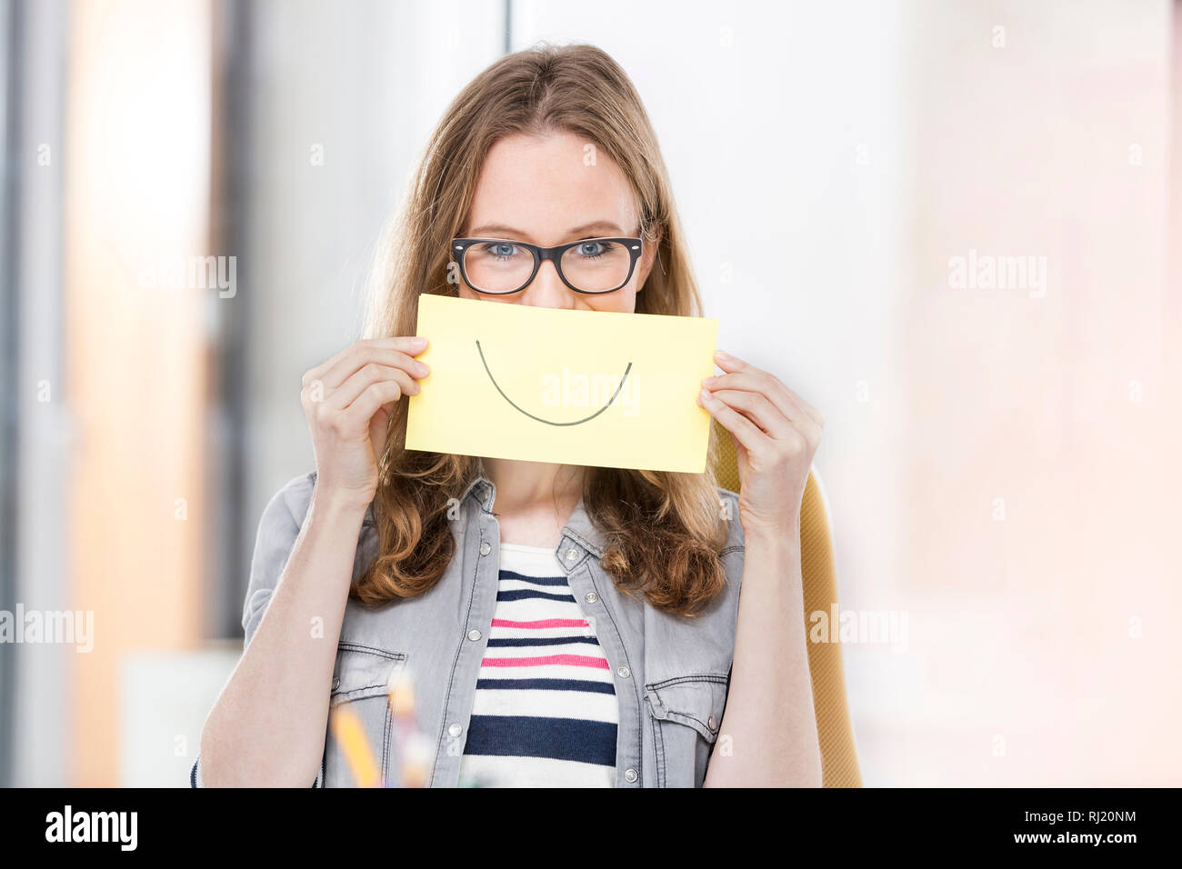 Creative businesswoman holding paper with smile drawn on it Stock Photo