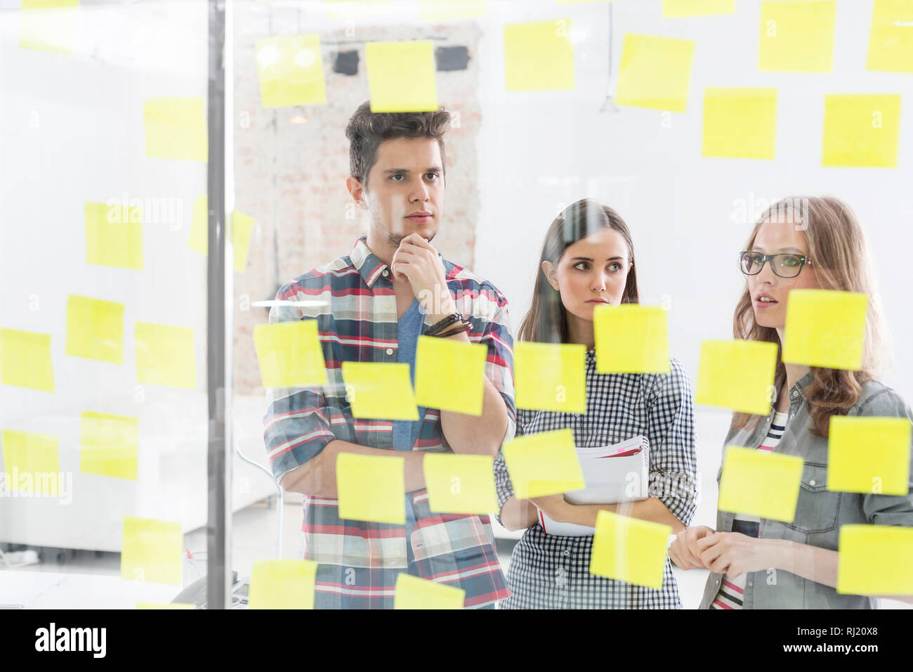 Creative business colleagues discussing over strategies on adhesive notes Stock Photo