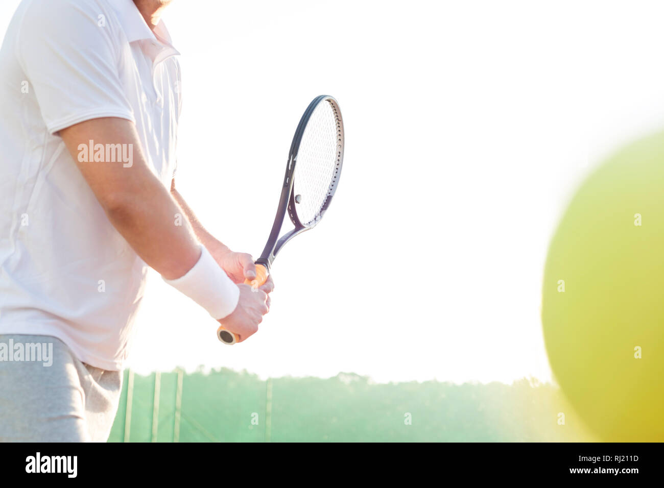 Midsection of mature man hitting tennis ball against clear sky Stock Photo