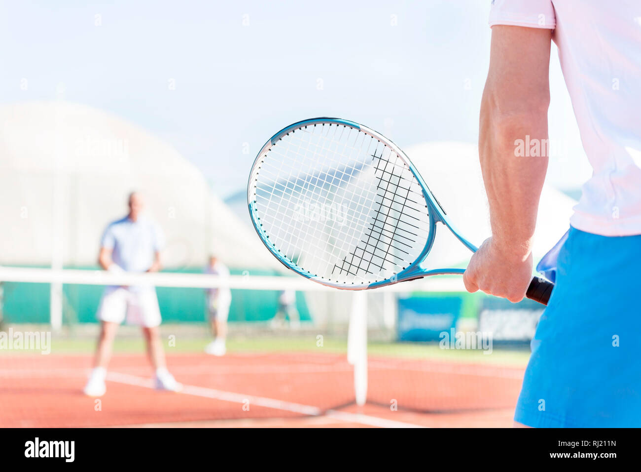 Midsection of mature man holding racket while playing with friends on tennis court Stock Photo