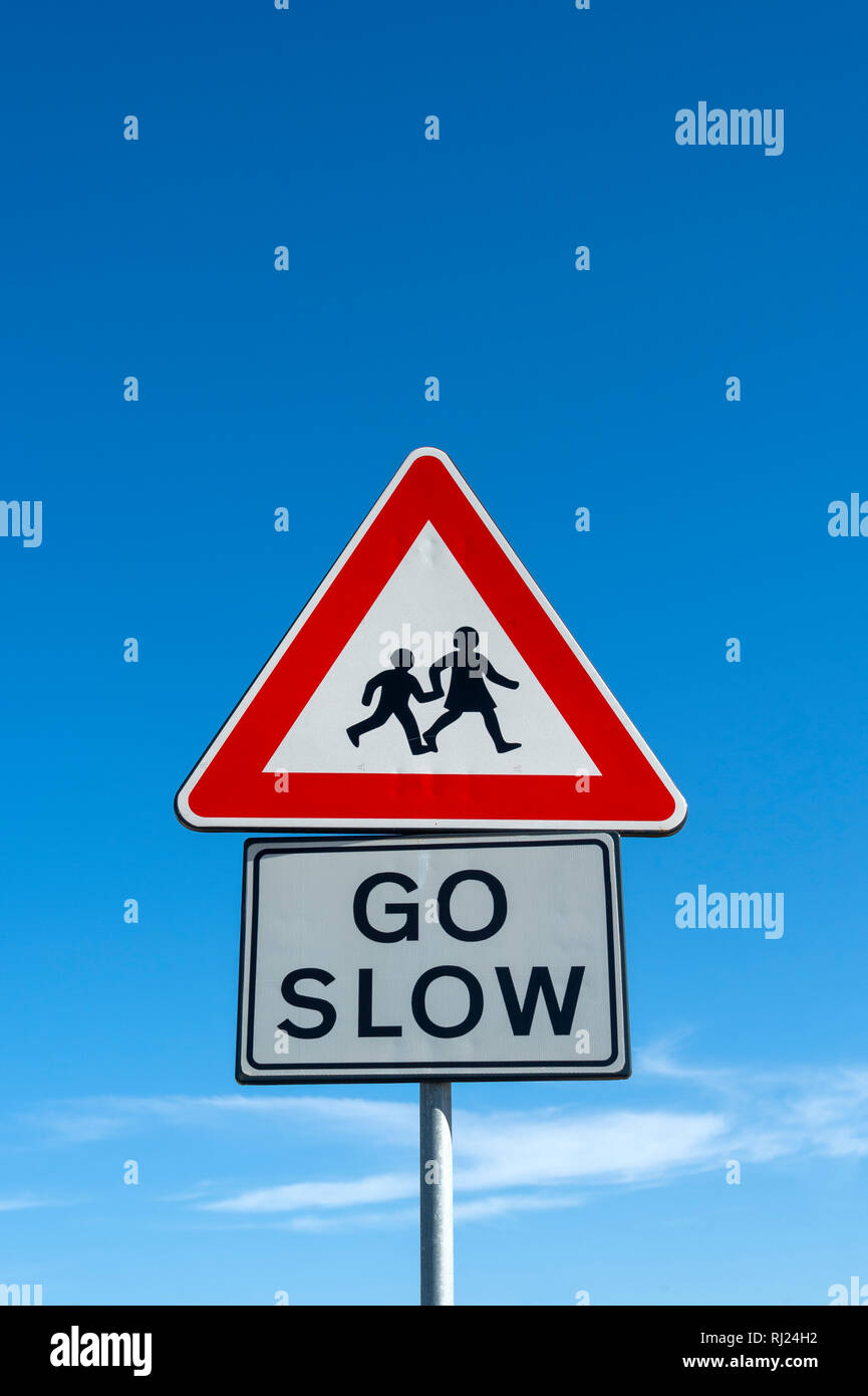 children crossing, go slow warning sign against a blue sky background Stock Photo