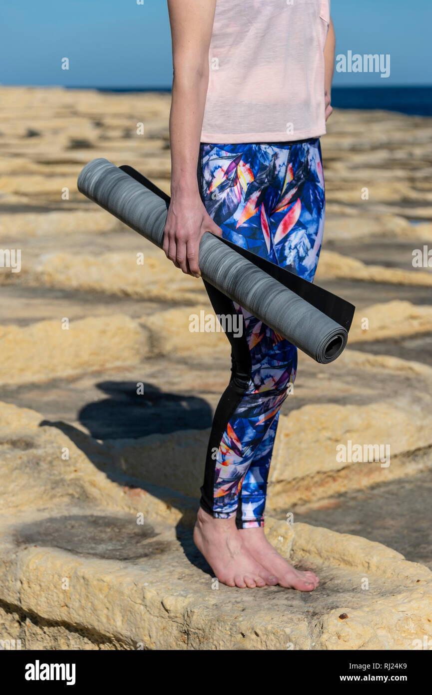 close up of a woman carrying a rolled up yoga mat outside in the sun