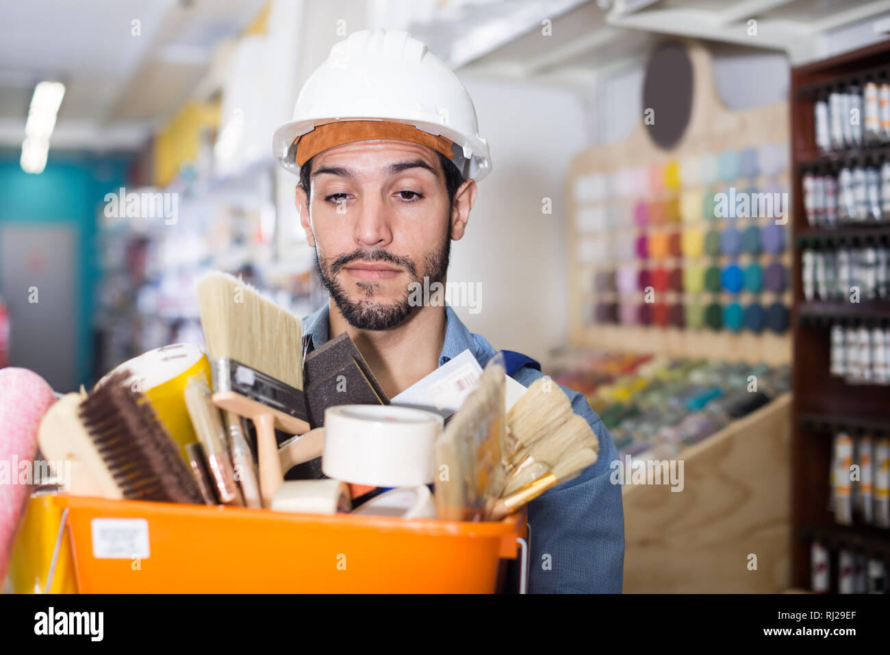 Young workman holding basket with picked tools in paint store Stock Photo