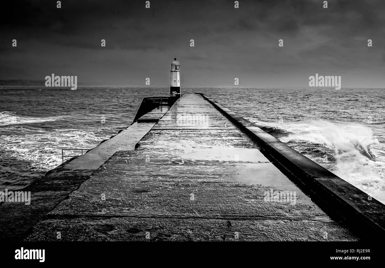 Road to lighthouse surrounded by crashing, stormy waves in dramatic black and white Stock Photo