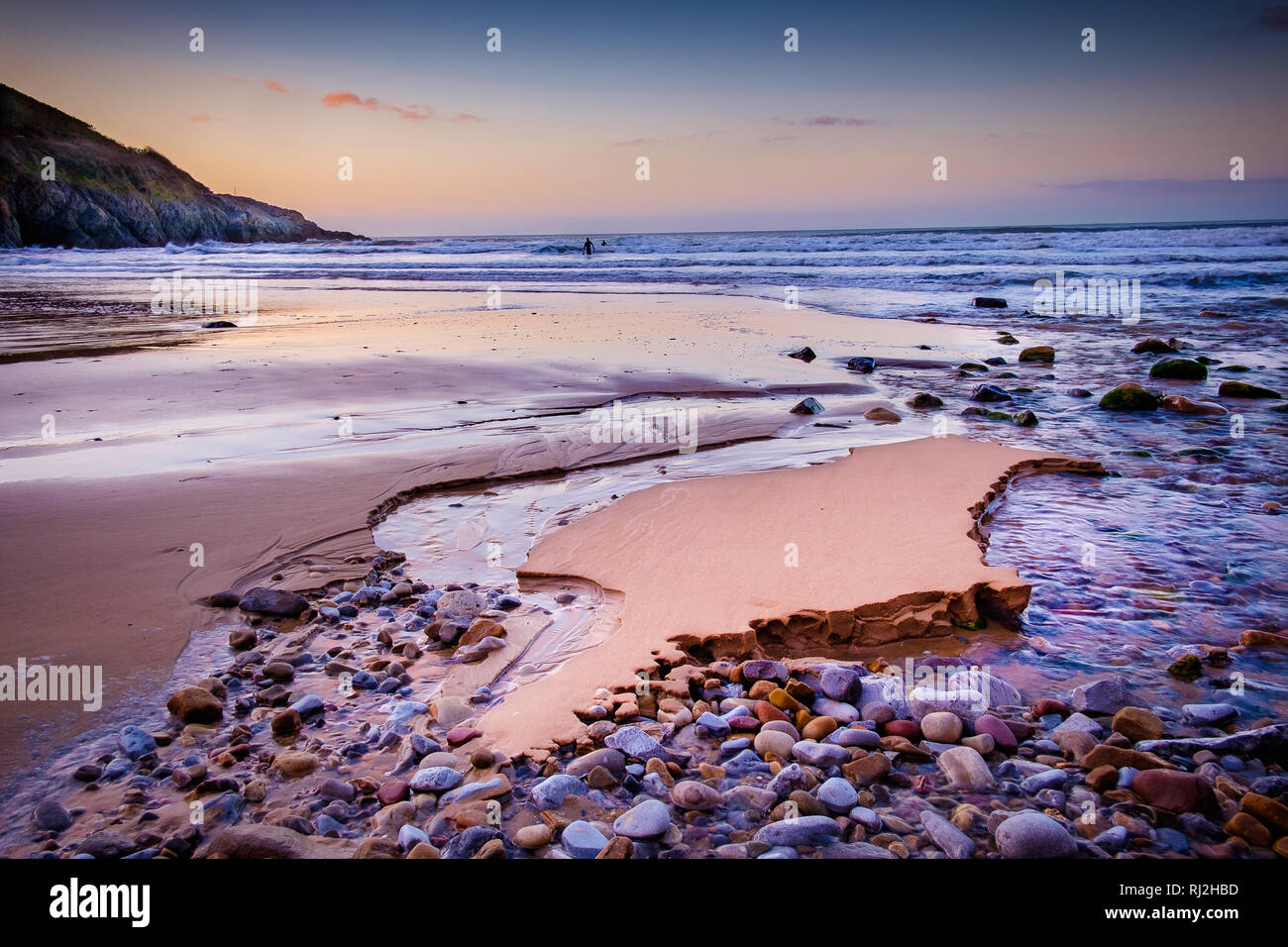 Pastel sunset over Caswell Bay with the tide out and tributary running down over pebbles Stock Photo