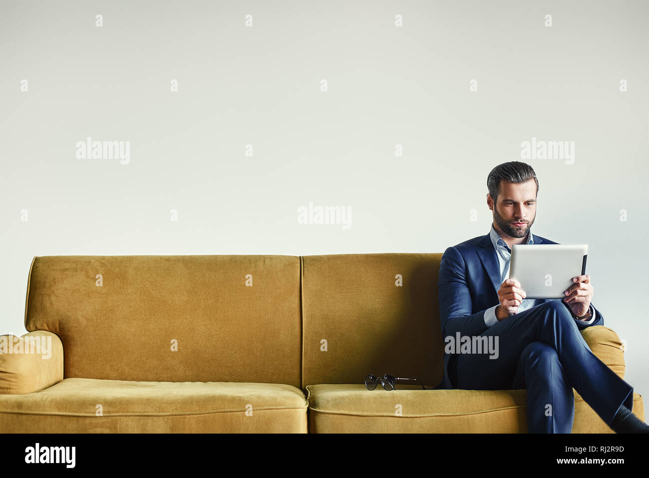 Multitasking...Busy businessman is working with touchpad while sitting on the couch in office. Business look. Stock Photo