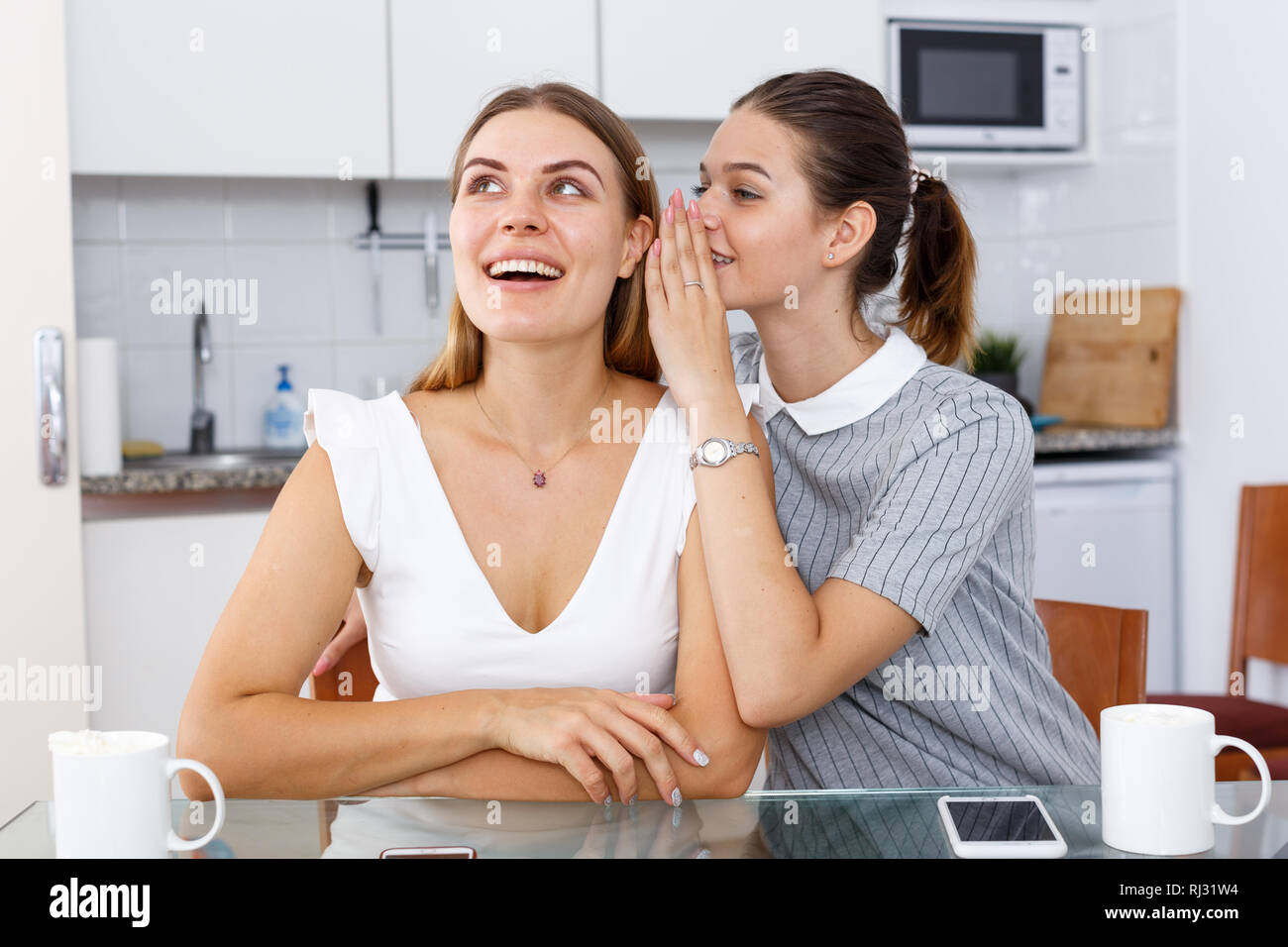 Two young girls friends whispering in kitchen interior Stock Photo - Alamy