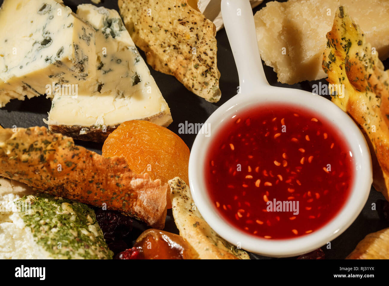 Look from above at bowl with cranberry sauce standing between pieces of cheese on black plate Stock Photo