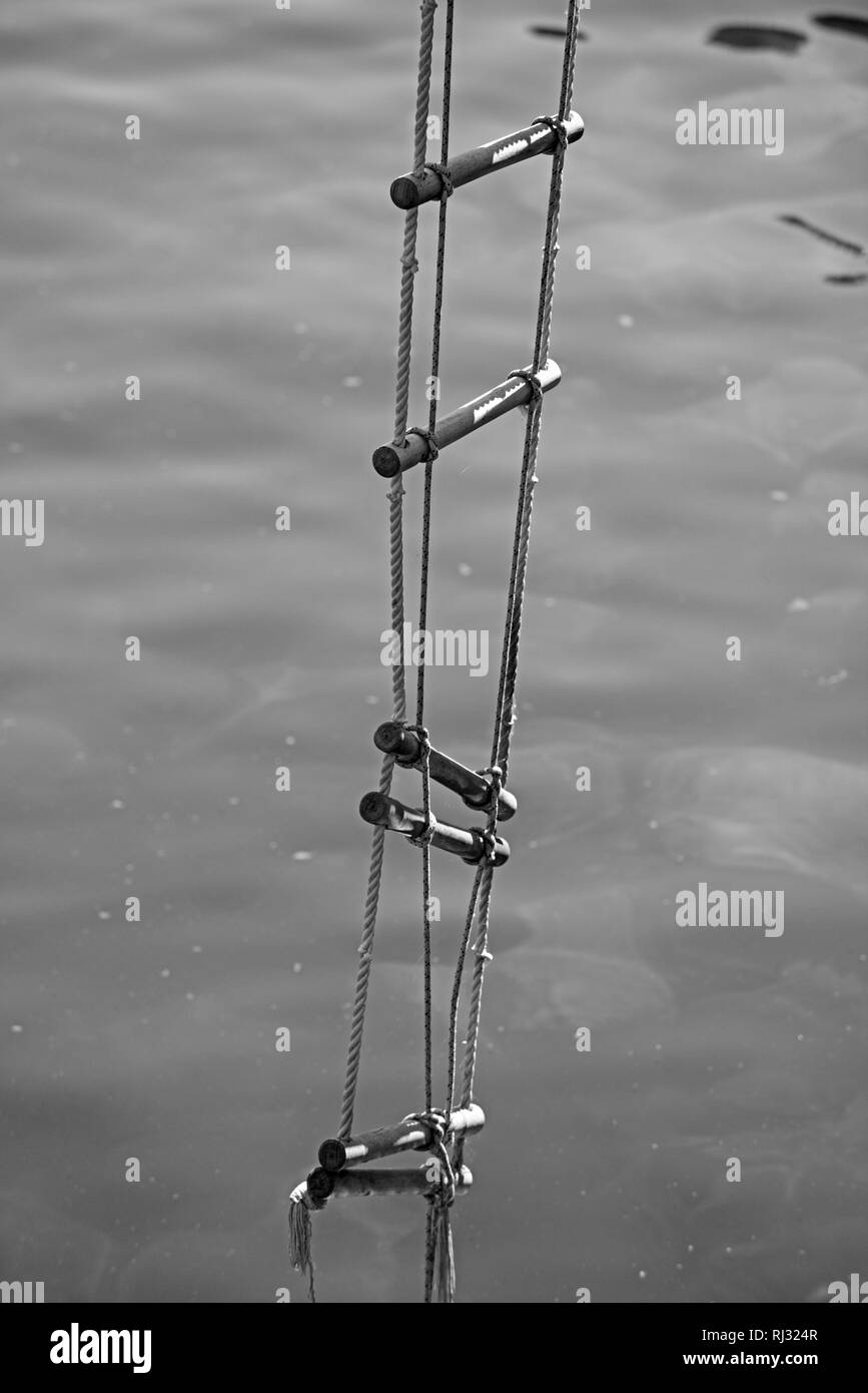 Achieving success. Rope ladder. Jacobs ladder. Rope ladder with wooden steps. Rope over water surface. Rescue or escape rope. Climbing the ladder of Stock Photo