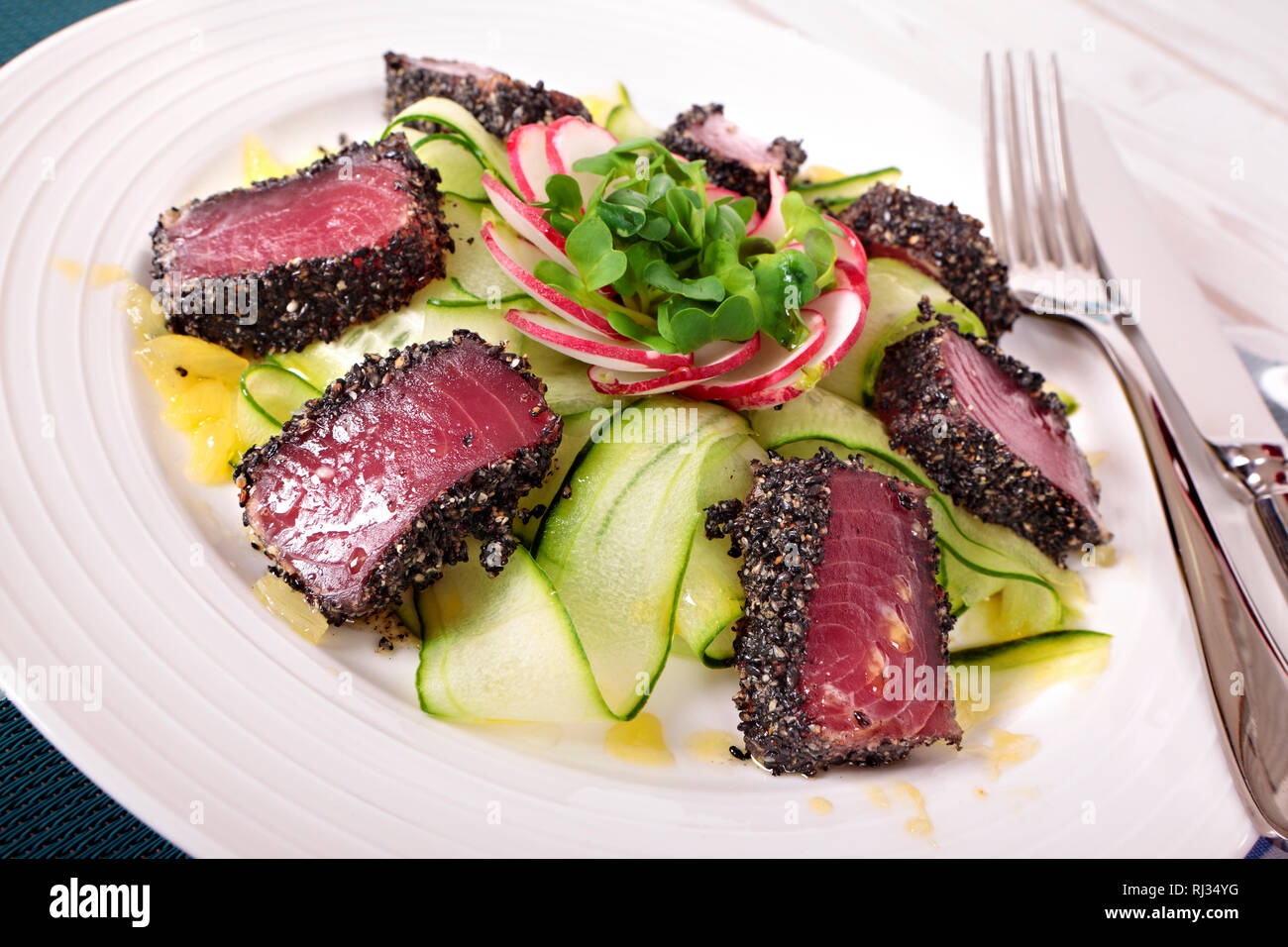 Seared Ahi tuna coated with sesame seeds and green salad on white plate