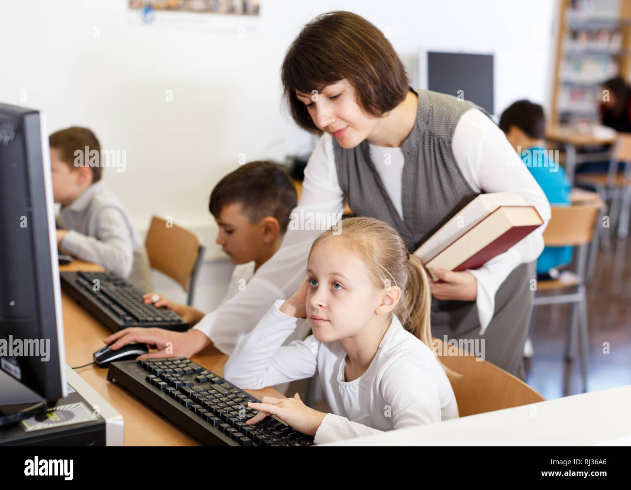 Young female teacher working with schoolgirl in computer class of ...