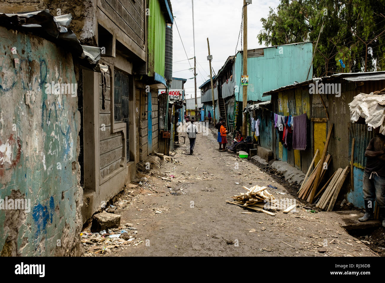 Urban poverty in Africa: People walk down a muddy street alongside tin houses in the Sinai slum in Nairobi, Kenya Stock Photo