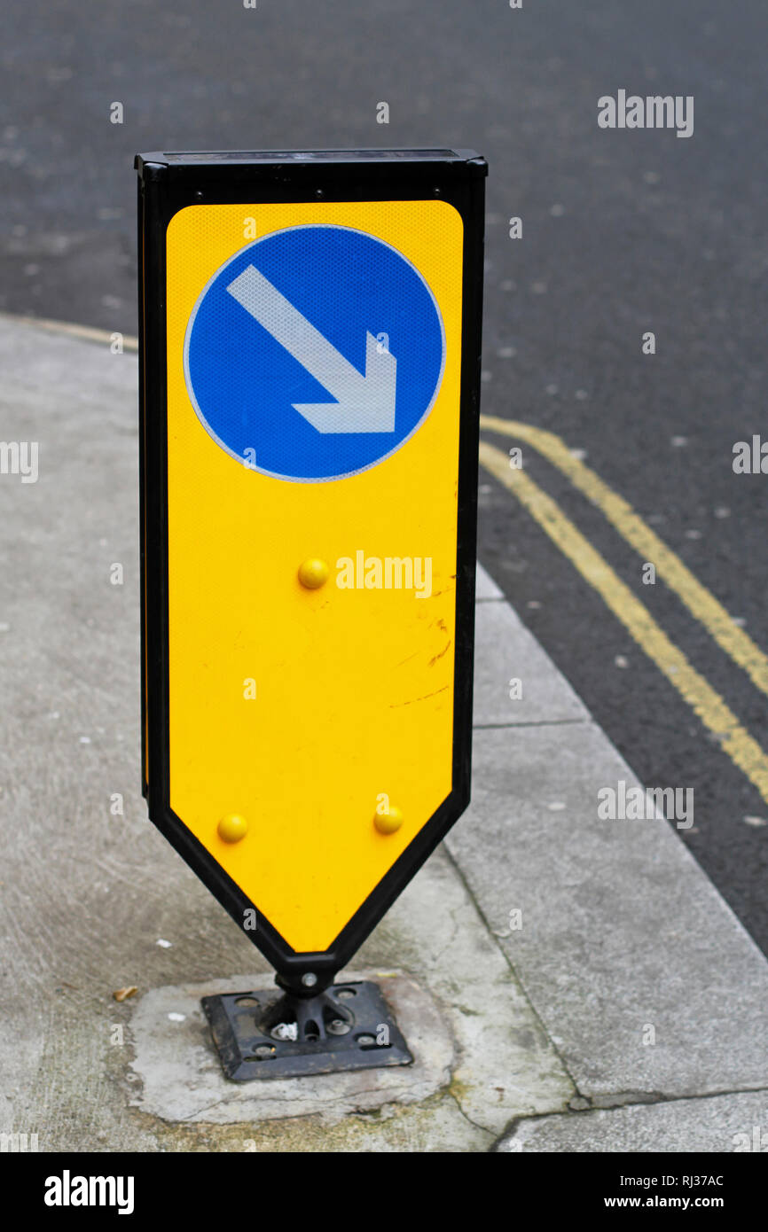 Blue arrow direction sign at yellow post Stock Photo - Alamy