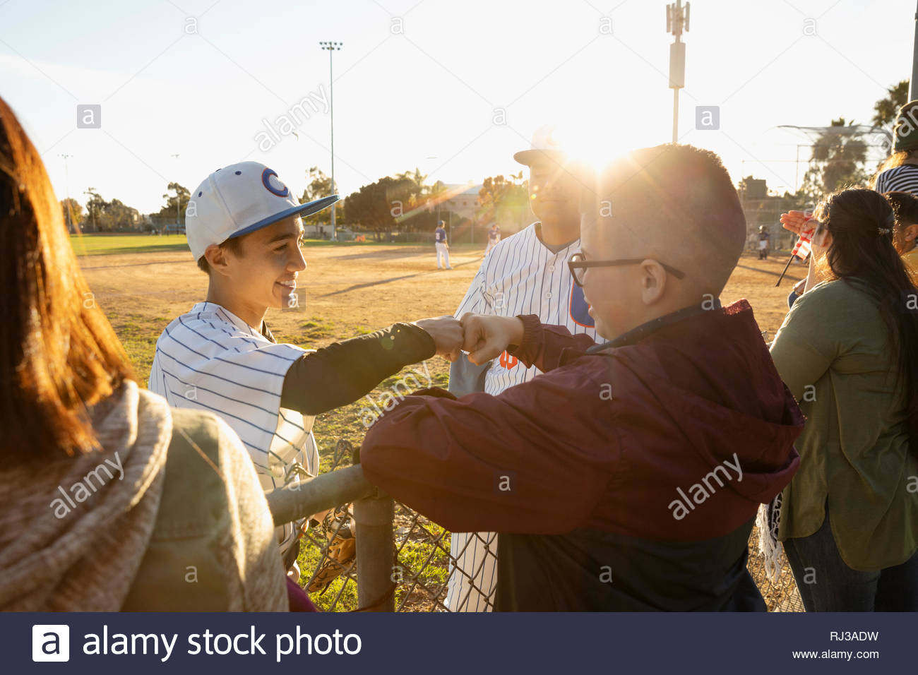 Baseball player fist bumping friend at sunny fence Stock Photo