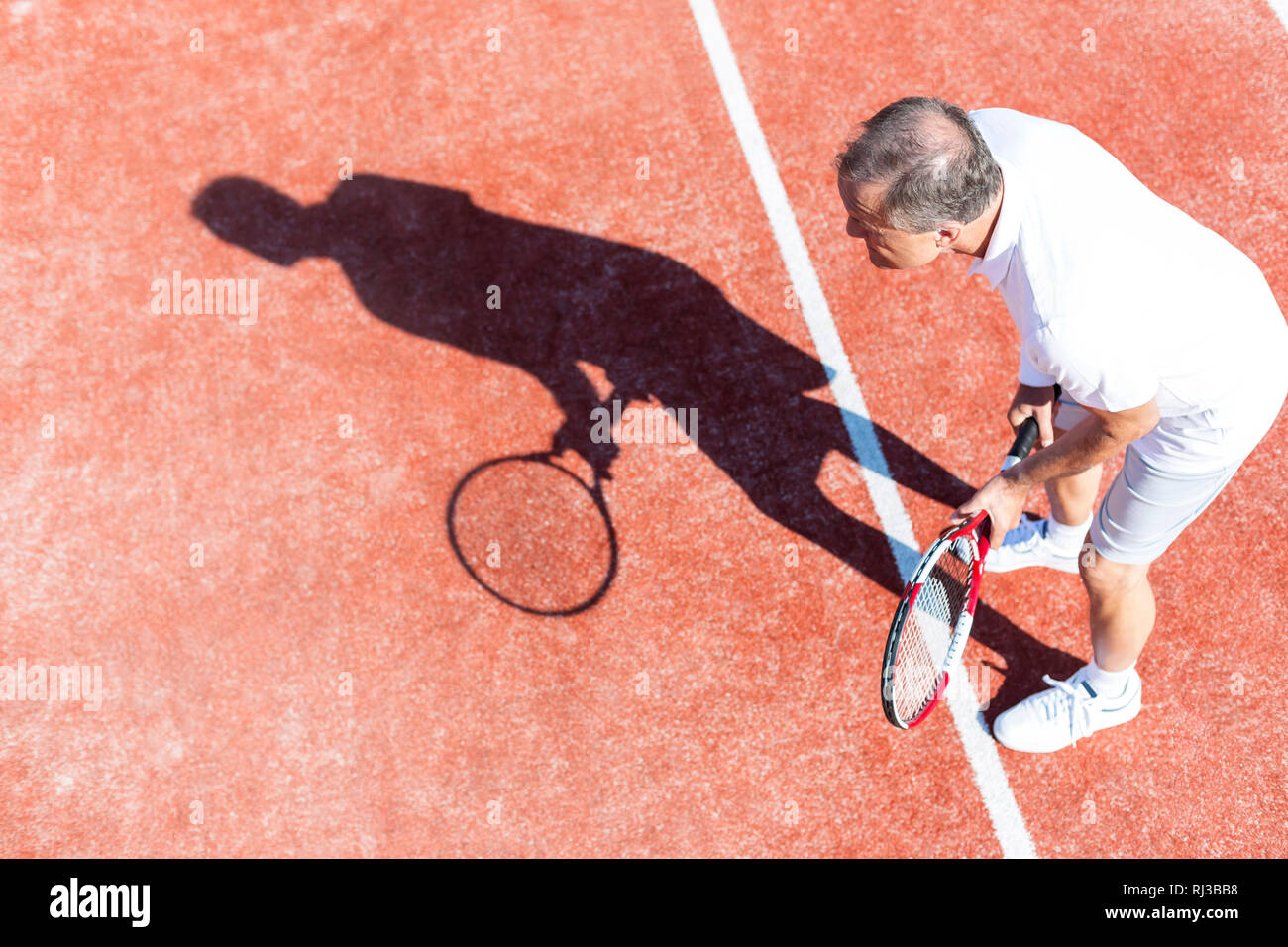 Full length of senior man playing tennis on red court during summer weekend Stock Photo
