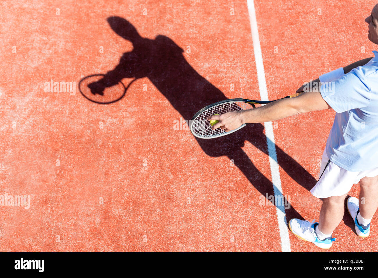 High angle view of mature man serving tennis ball on red court Stock Photo