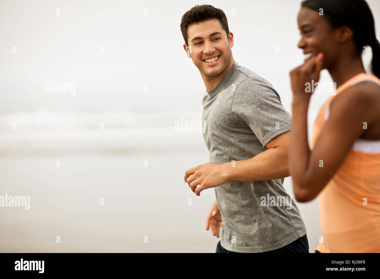 Smiling young couple jogging together on a beach. Stock Photo