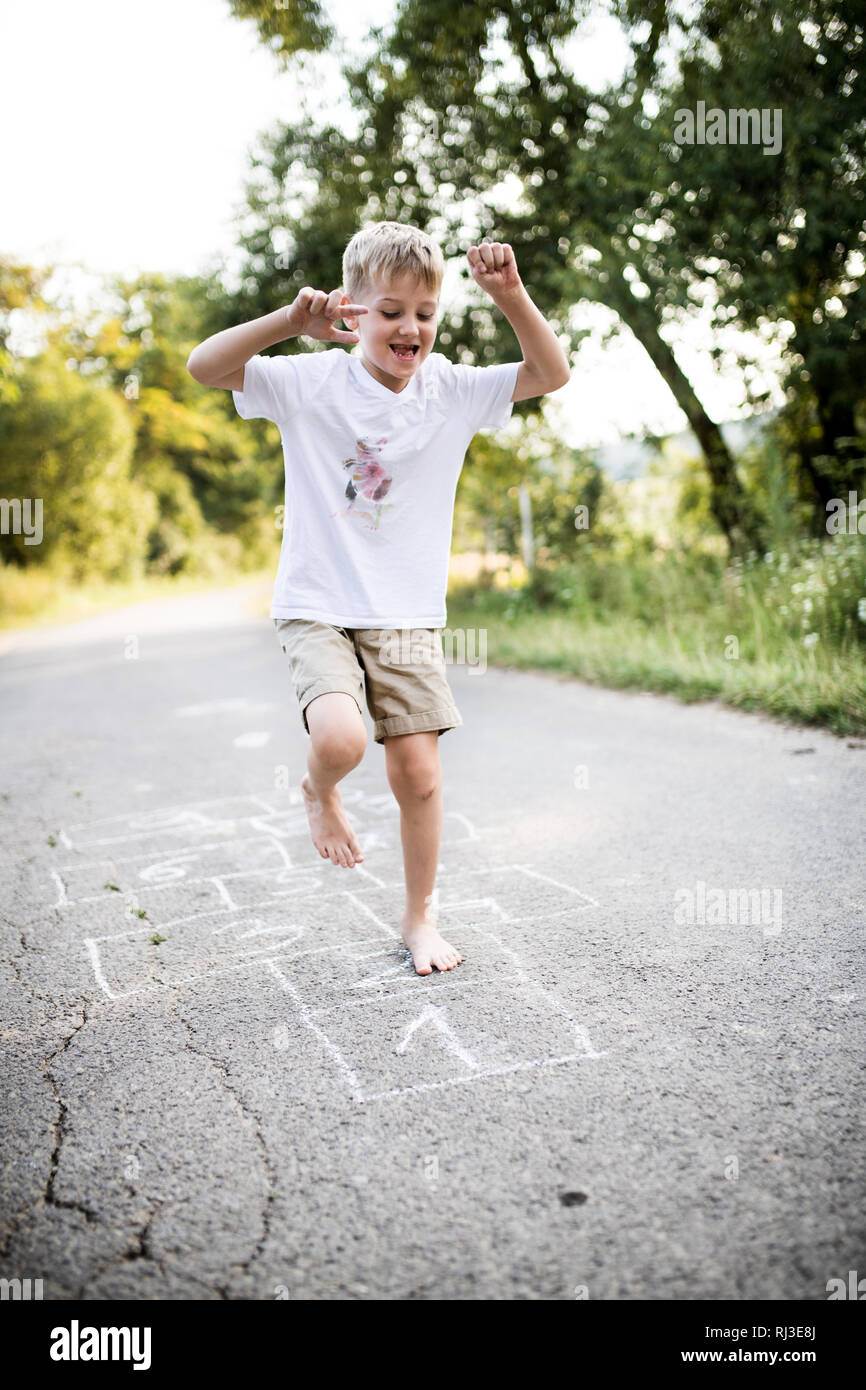 A small boy hopscotching on a road in park on a summer day. Stock Photo