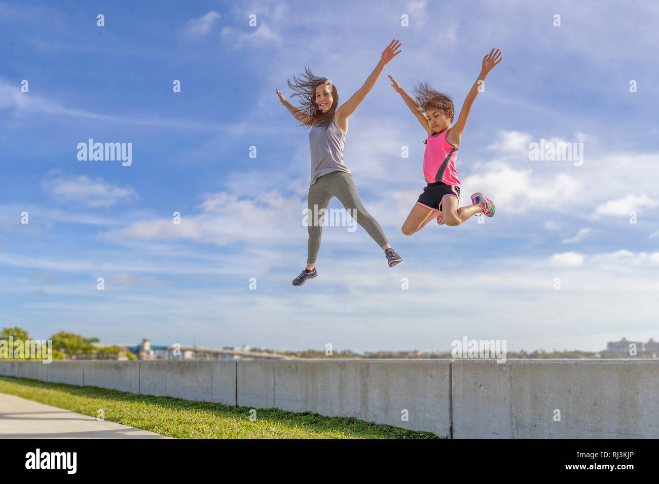 Mother and daughter challenge to see who can jump the highest from the seawall on a bright sunny day. Stock Photo