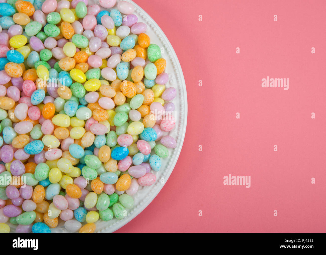 Many colorful candy jelly beans on porcelain plate laying on light pink