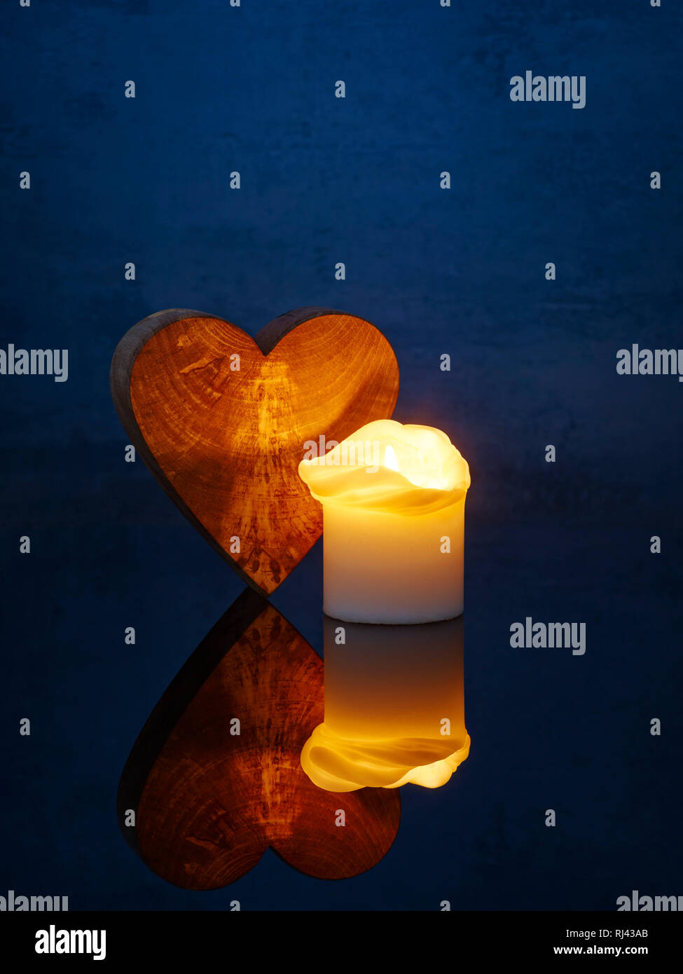 Kerze mit Spiegelung angez?ndet auf einem Tisch und Herz aus Holz Stock Photo