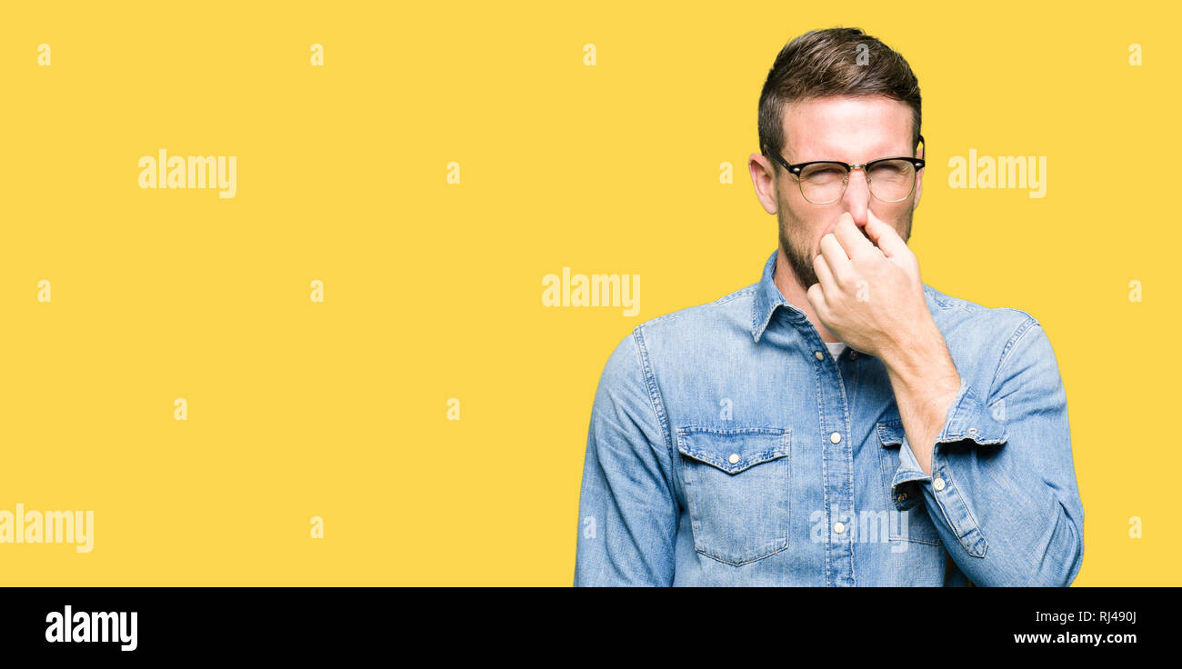 Handsome man wearing glasses smelling something stinky and disgusting