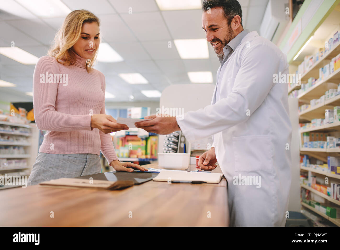 Male chemist taking prescription from female customer at pharmacy. Customer handing a medical prescription to the pharmacist standing behind counter. Stock Photo